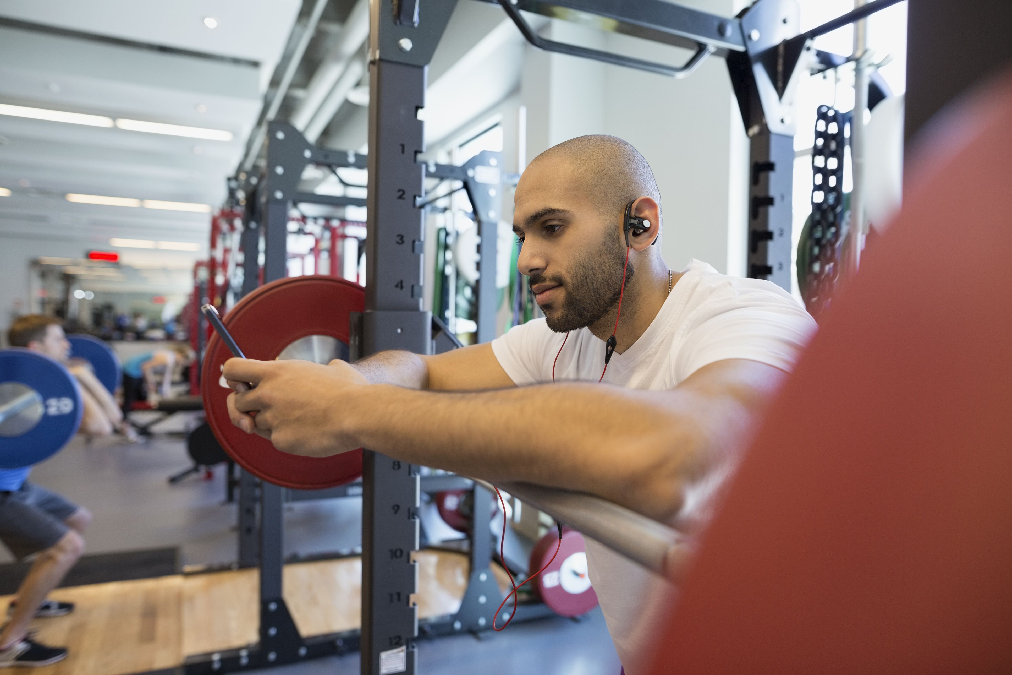 Man using cell phone at barbell in gym Man using cell phone at barbell in gym