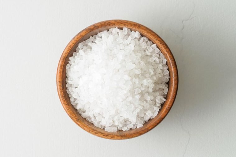 Wooden bowl with large sea salt on gray stone table. Top view, close up.