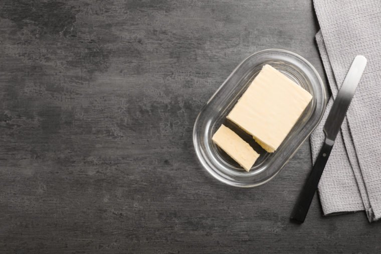 Plate with tasty fresh butter and knife on table, top view