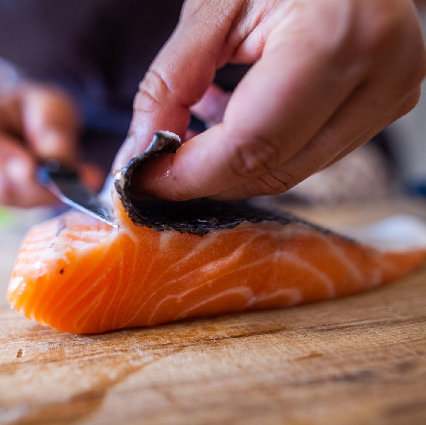 cette photographie présente en cuisine une personne en train de découper du poisson, notamment du saumon, un pavé